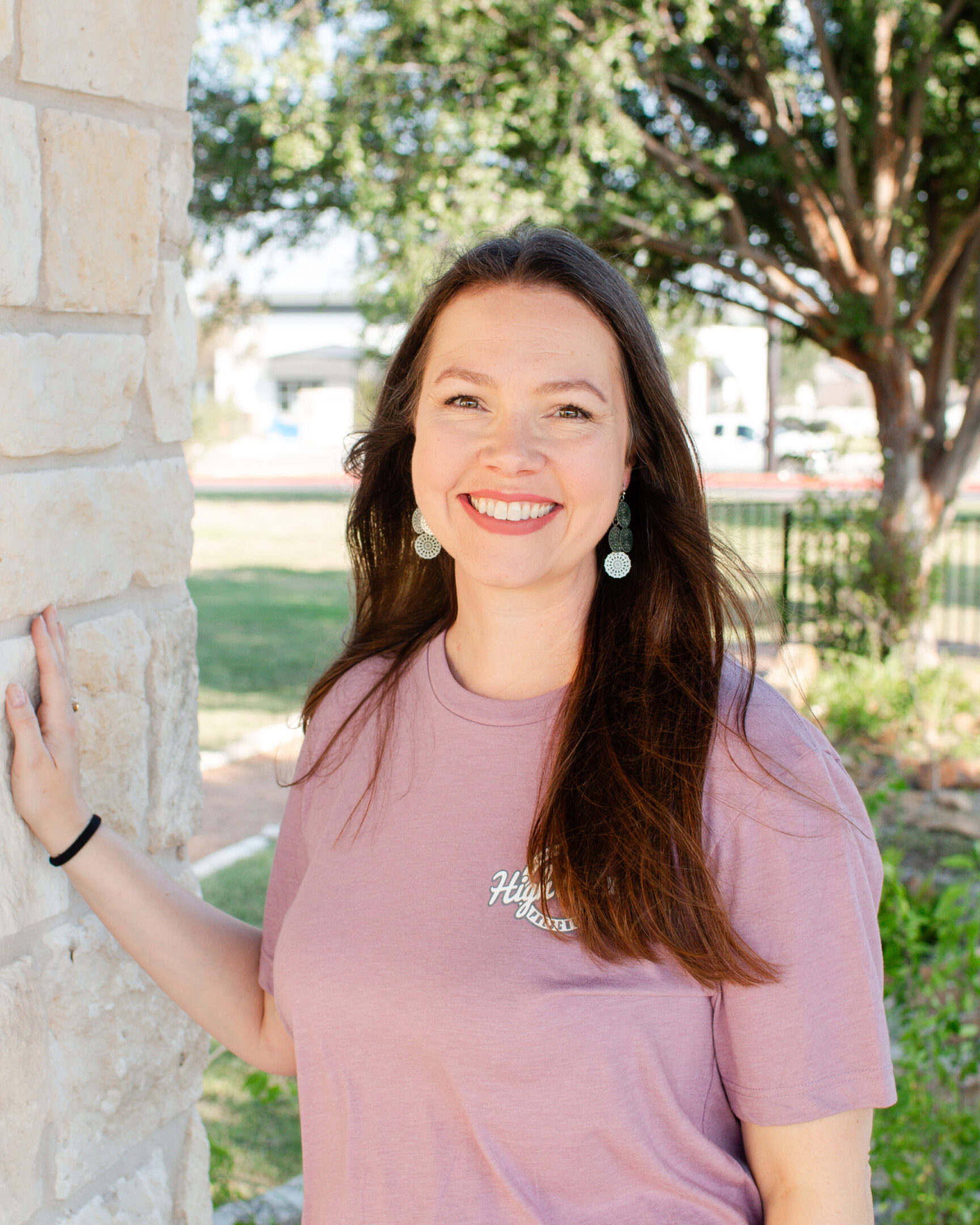 A woman in pink shirt standing next to a brick wall.