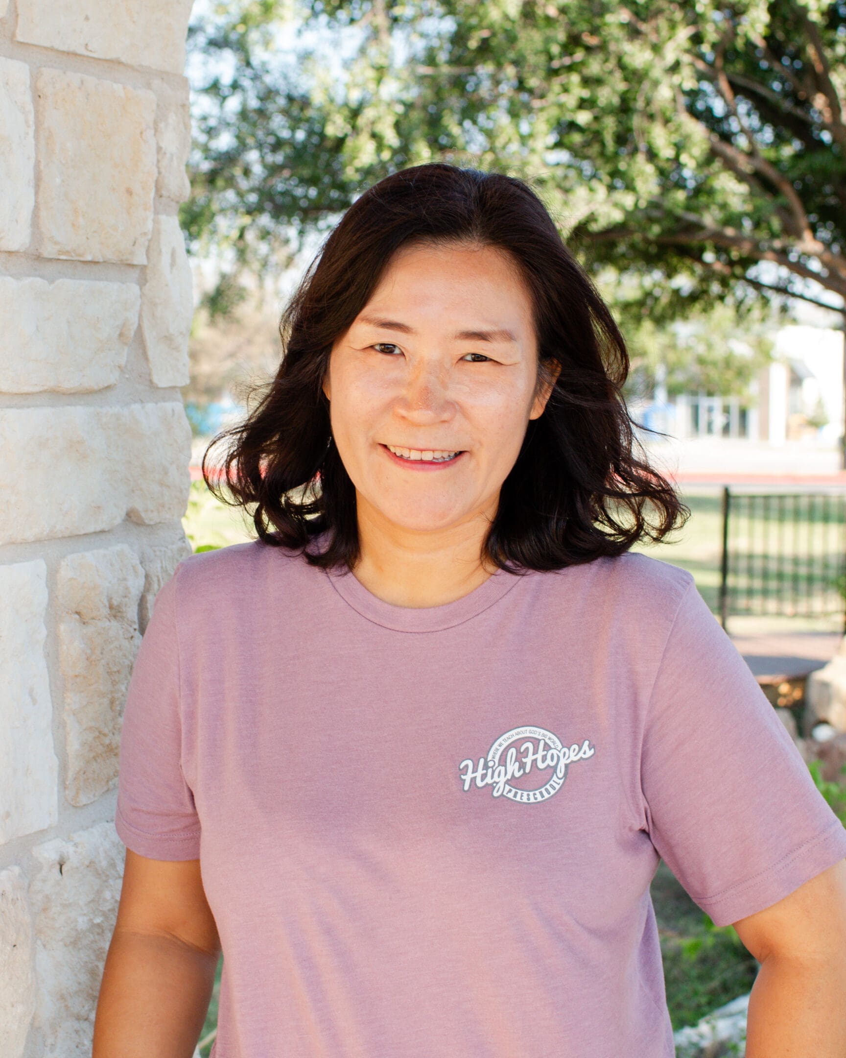 A woman in a purple shirt standing next to a brick wall.